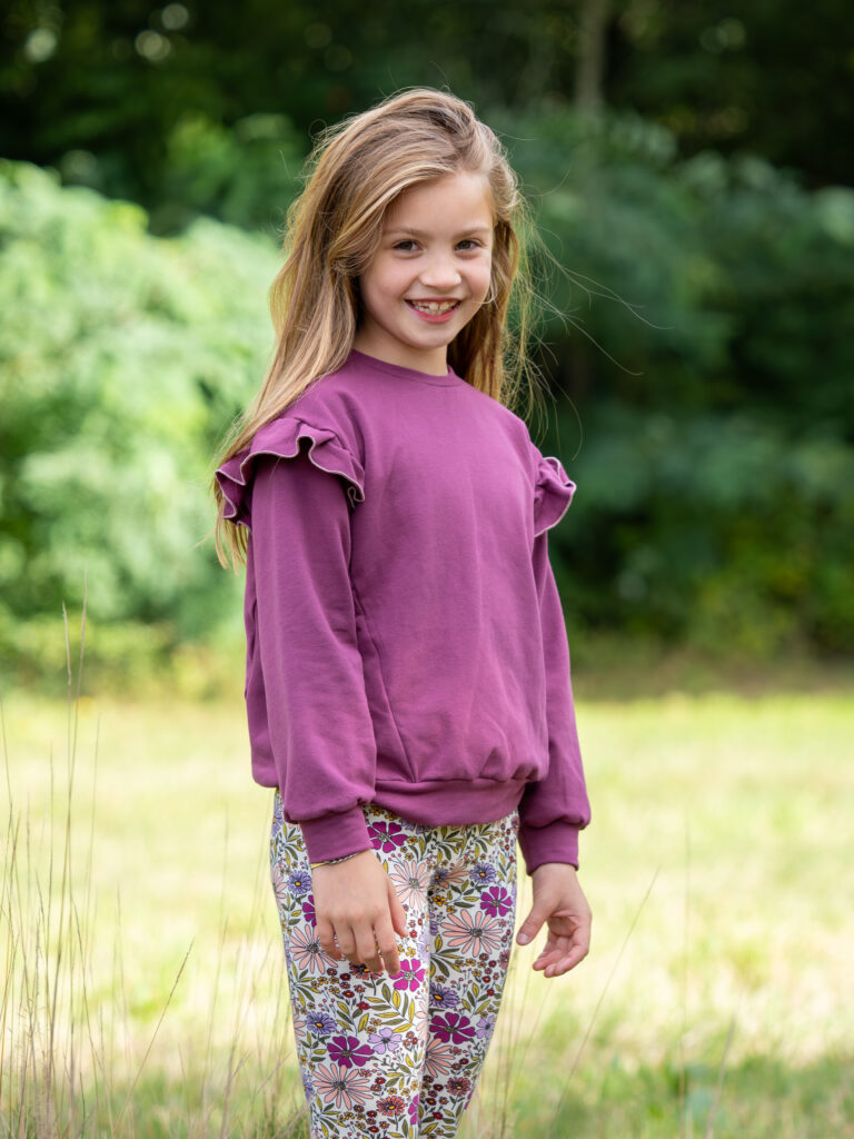 meisje met bloemen legging aan en een aubergine kleurige trui.