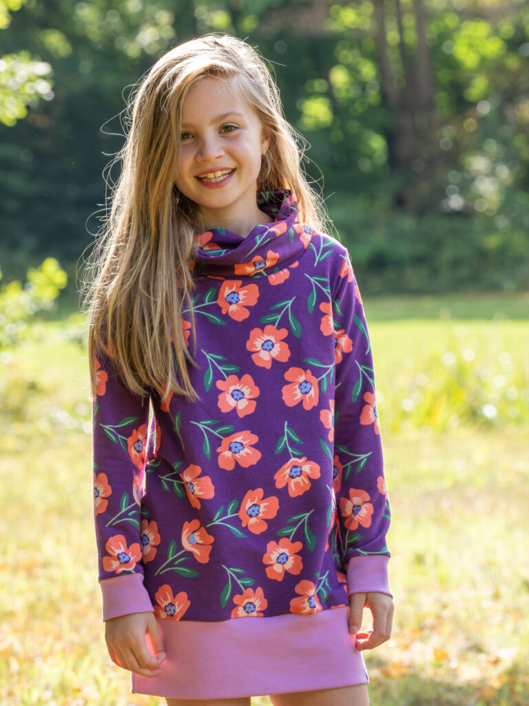 meisje met sweat jurk aan met grote koraal kleurige bloemen op een donker paarse achtergrond