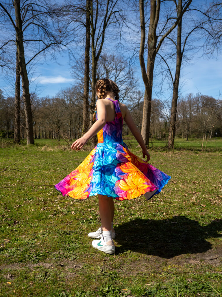 Model draaiend in regenboog halterjurk kinderen met zwierige cirkelrok en vrolijke kleuren