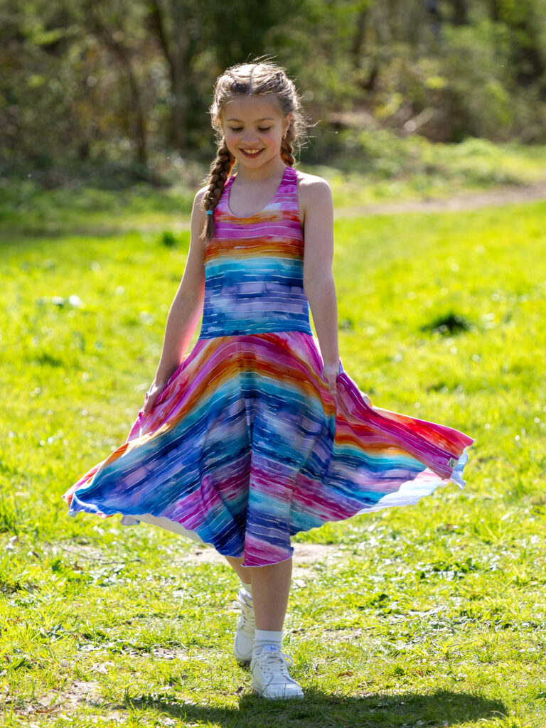 Halterjurk kinderen met pastel regenboog streepjes gedragen door model, zwierige cirkelrok en comfortabele pasvorm
